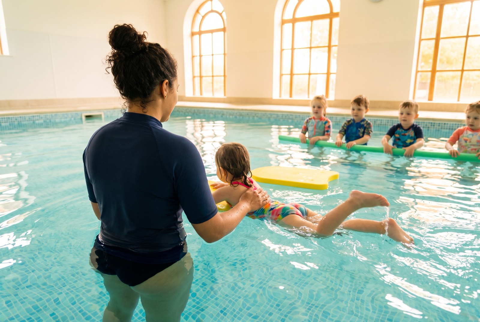 Professora dando aula de natação para crianças em piscina rasa e clara